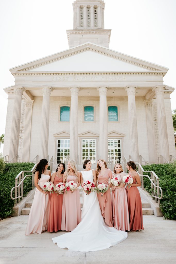 Bride laughs with bridesmaids in pink dresses outside of Family Church Downtown West Palm Beach Florida