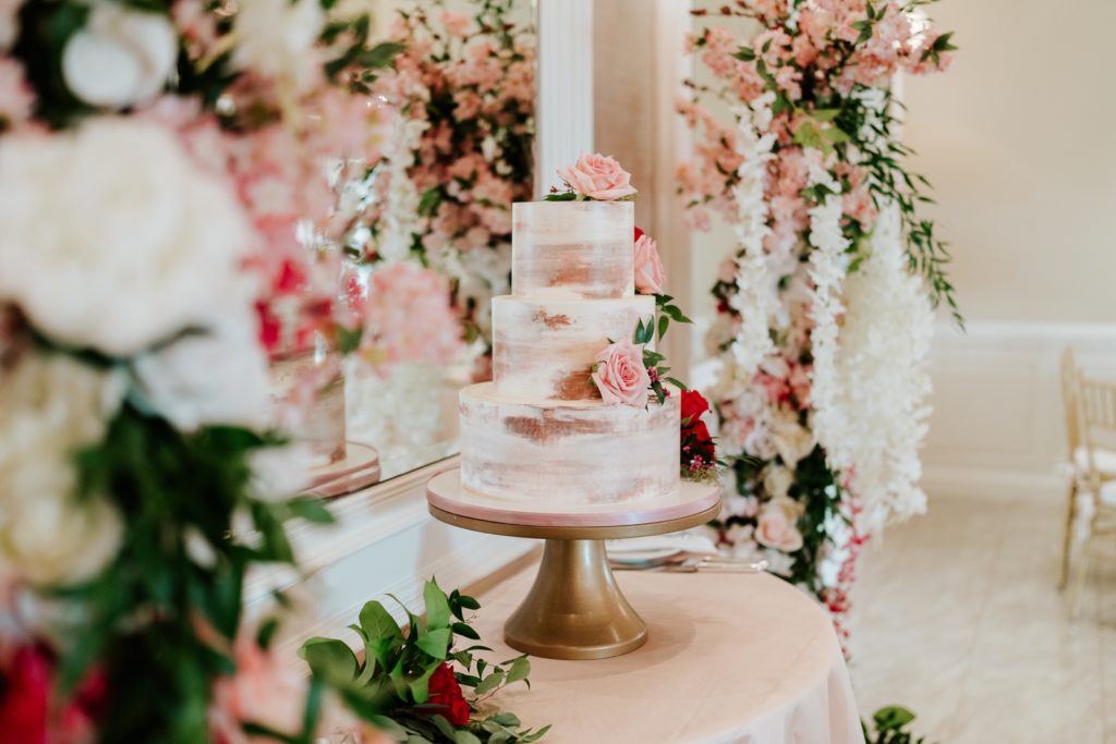 Breakers West wedding reception cake in front of mirror surrounded by pink and red roses
