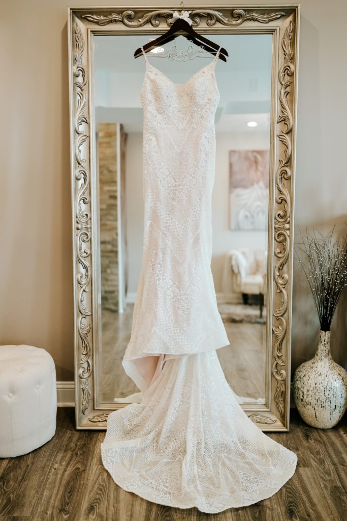 Lace L&H Bridal wedding dress hanging on mirror at Pellegrino's Salon & Suite