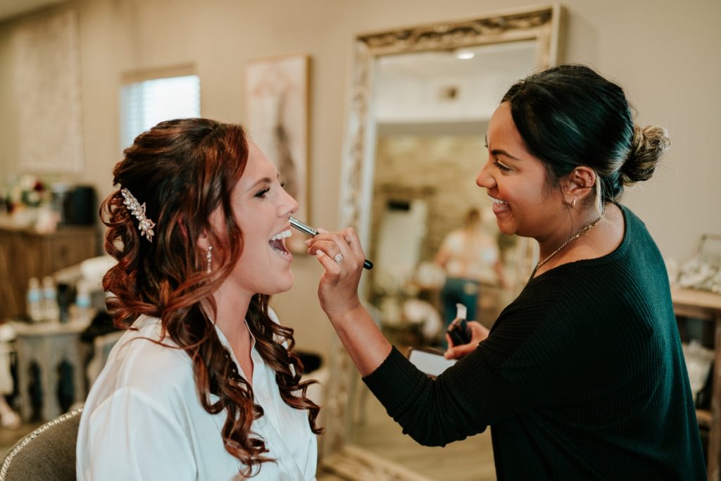 Bride laughs as makeup artist applies bridal makeup at Pellegrino's Salon & Suite