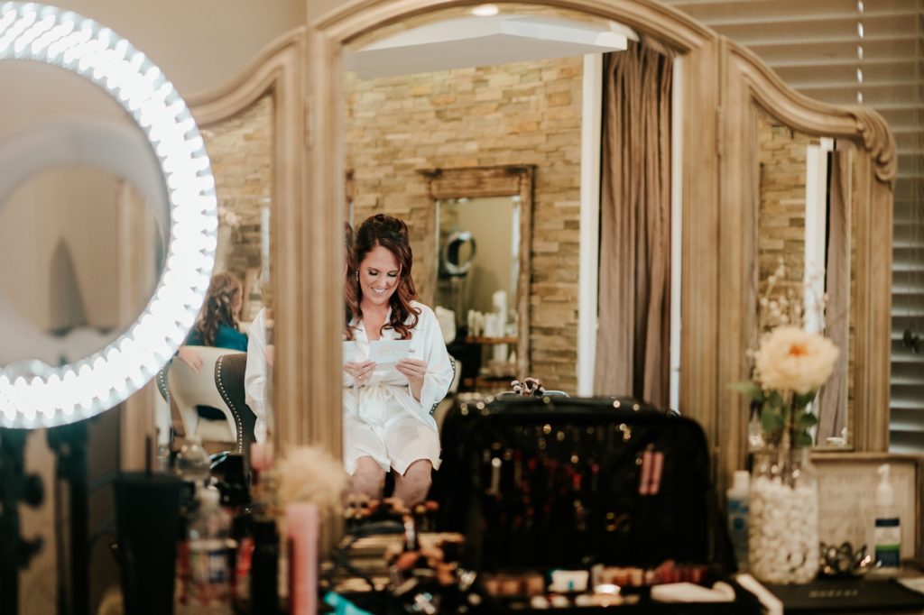 Reflection in mirror of bride reading letter from groom on wedding day in Pellegrino's Salon & Suite
