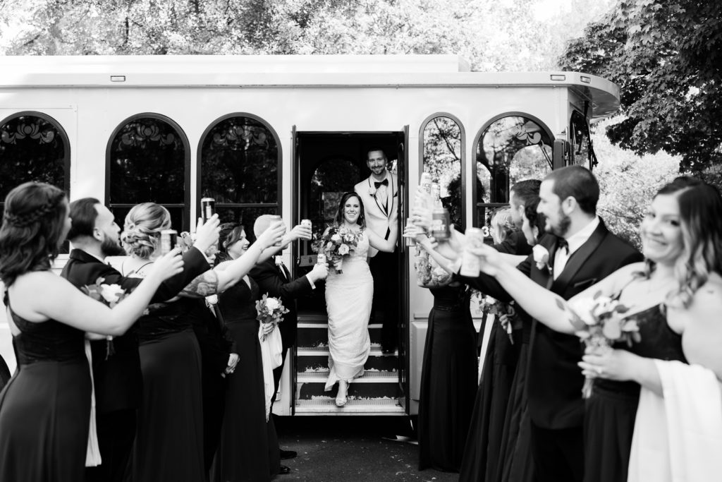 Bride and groom exit wedding trolley surrounded by wedding party