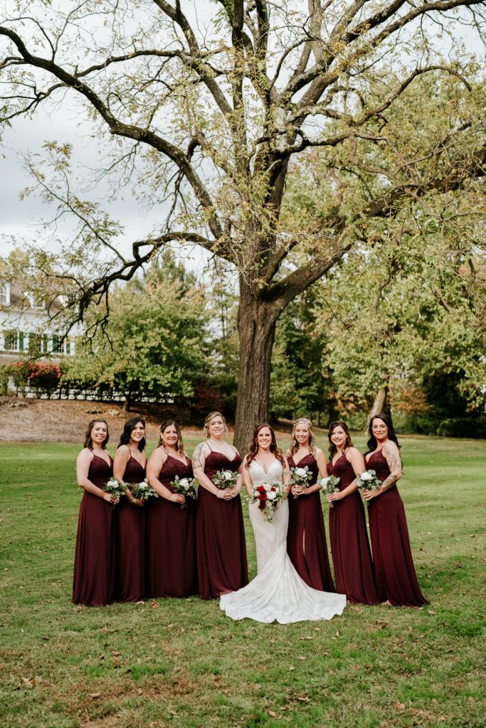 Bride poses with bridesmaids under tree at Bensalen Township Country Club wedding