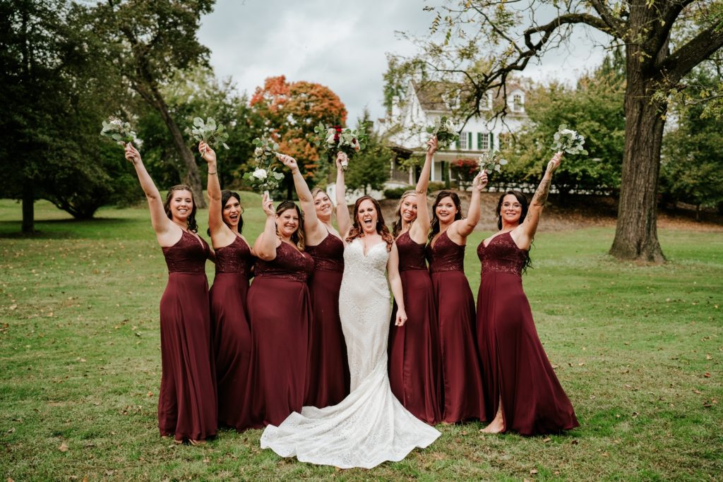 Bride and bridesmaids cheer with bouquets in the air at Bensalen Township Country Club fall wedding