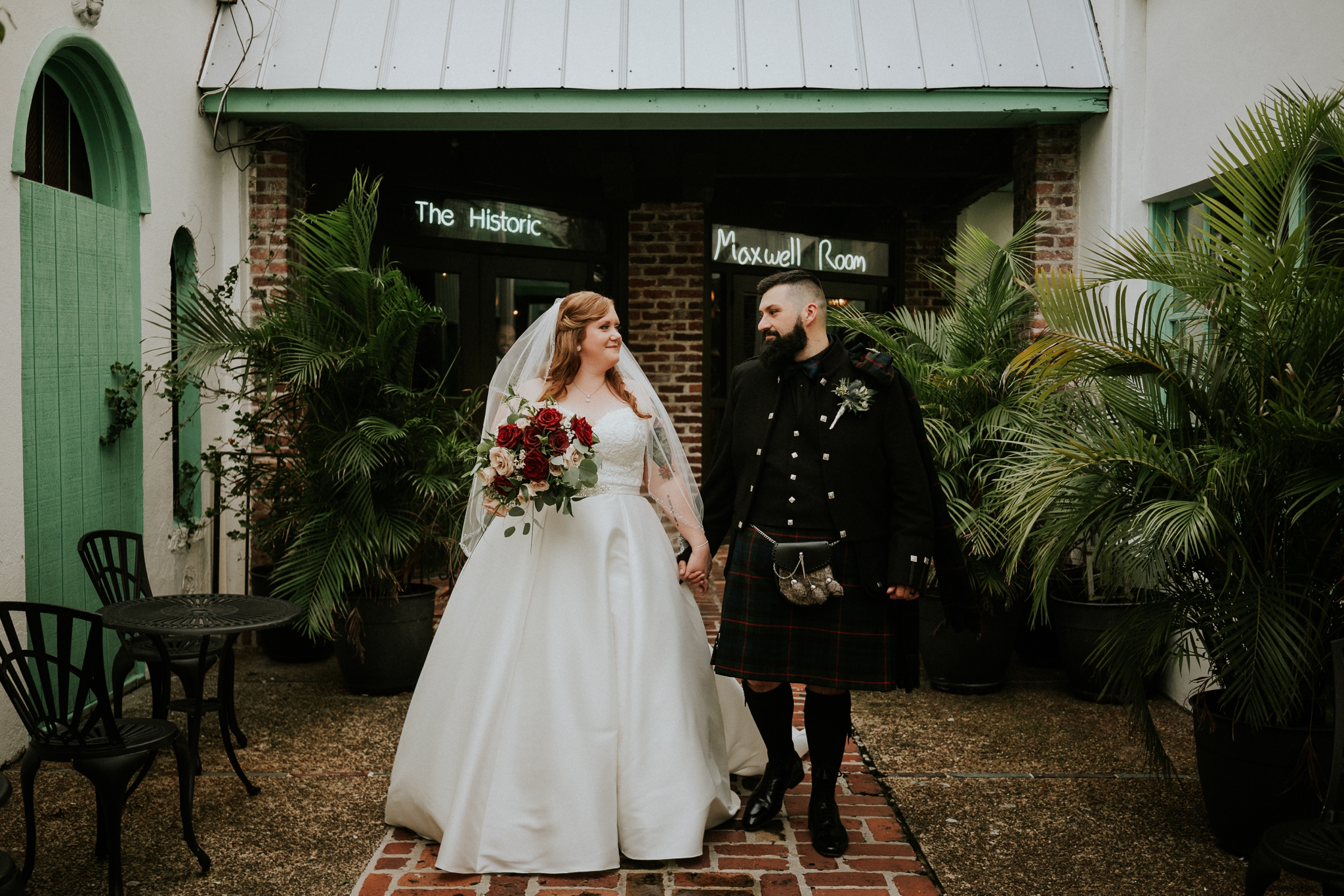 Fort Lauderdale newlyweds Allisha and Stan walk on brick path outside The Historic Maxwell Room courtyard with green neon sign lit above doors