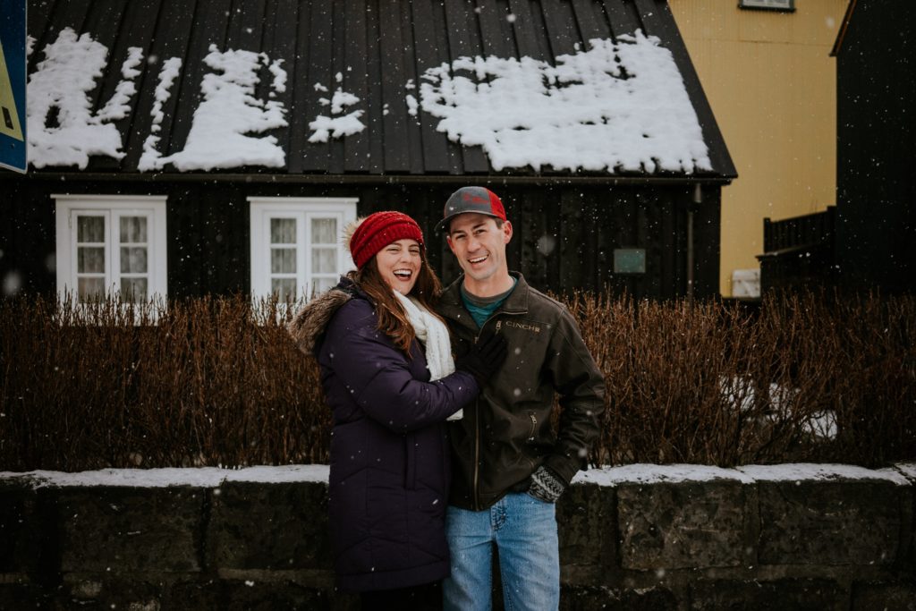 Couple stands in front of black house in the snow on street in Reykjavík Iceland