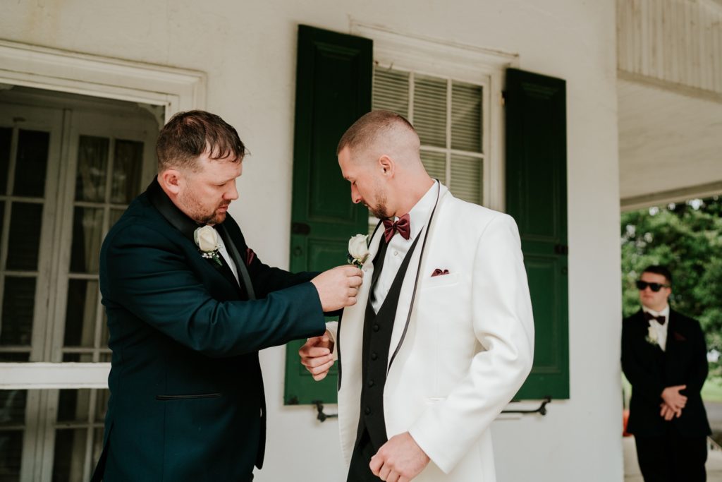 Best man pins boutonniere onto groom's white suit