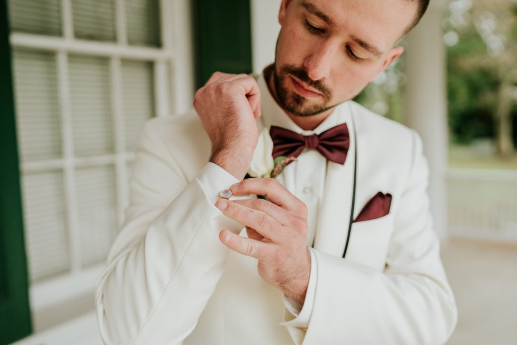 Groom in white suit puts on mother of pearl cuff links