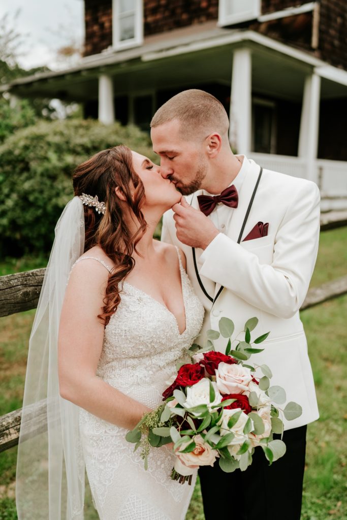 Groom brings bride's chin up for a kiss holding rose bouquet by Infinitely Yours Flowers