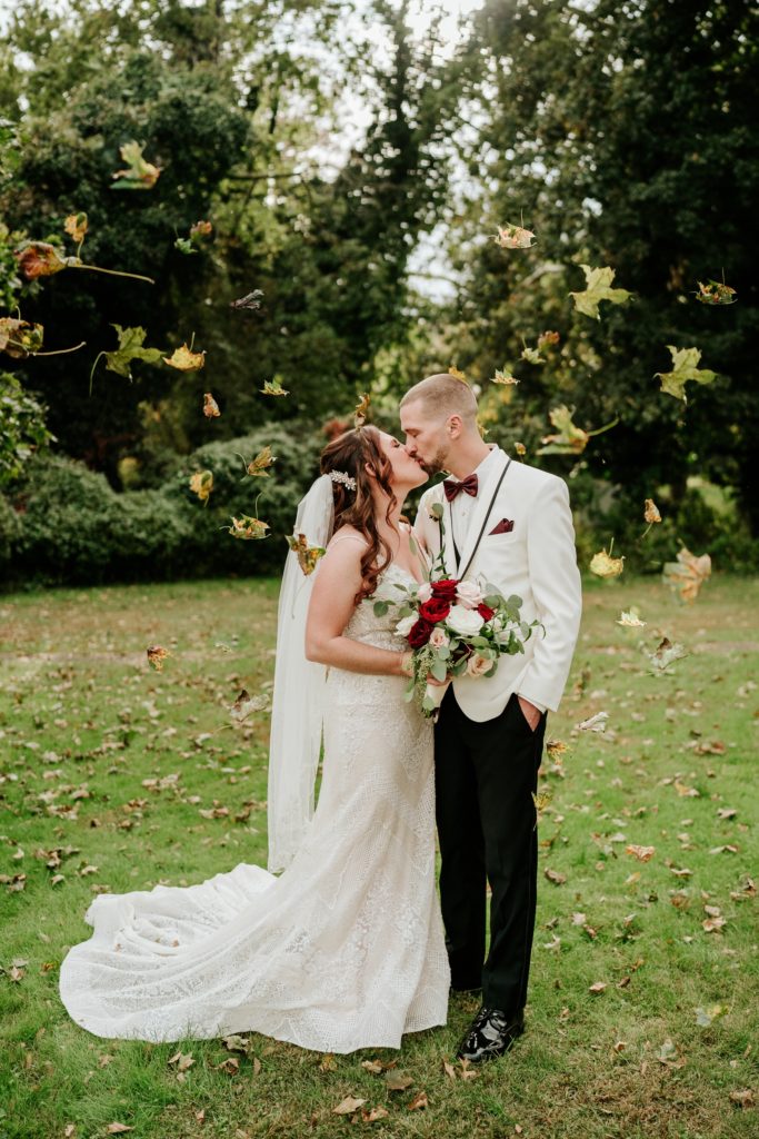 Bride and groom kiss under falling leaves at Bensalem Township Country Club fall wedding