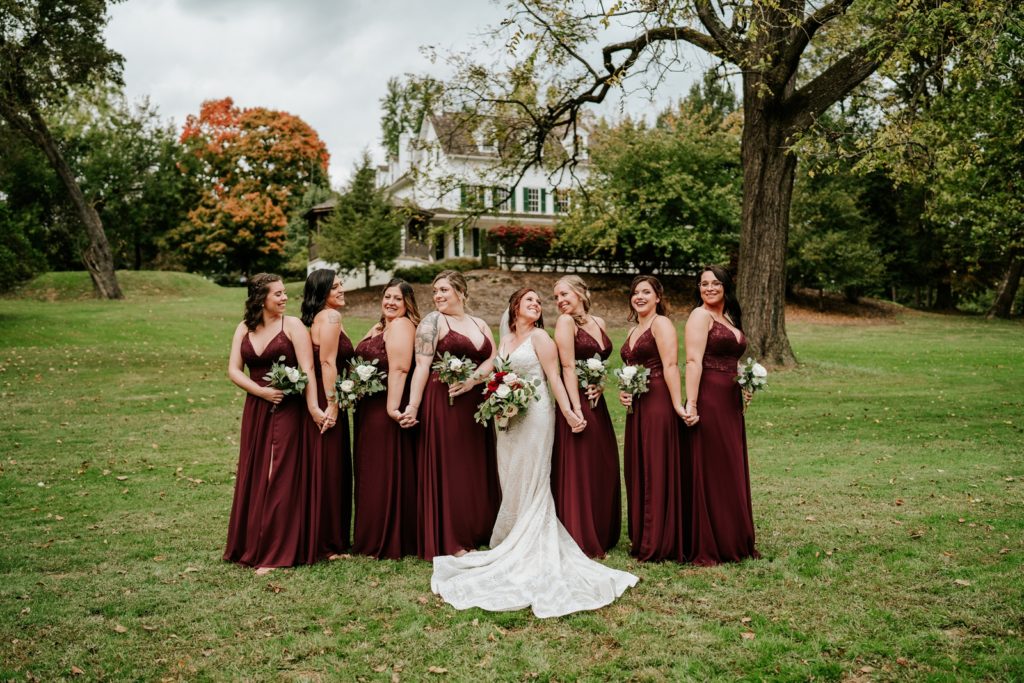 Bride and bridesmaids hold hands standing back to back at Bensalem Township Country Club fall wedding