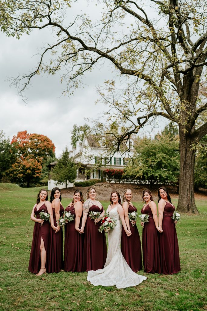 Bride and bridesmaids hold hands standing back to back at Bensalem Township Country Club fall wedding