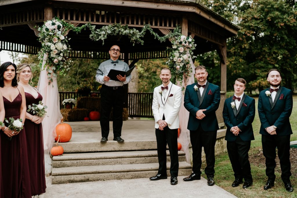 Groom and groomsmen smile under gazebo as bride walks down aisle