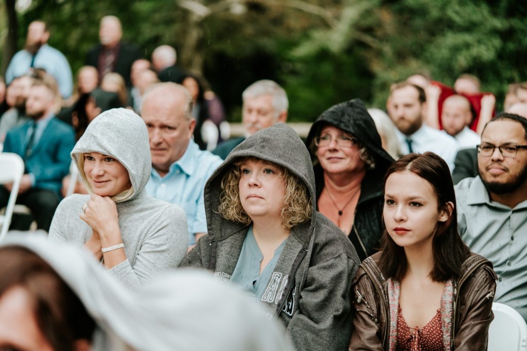 Guests hide under jacket hoods from the rain during wedding ceremony