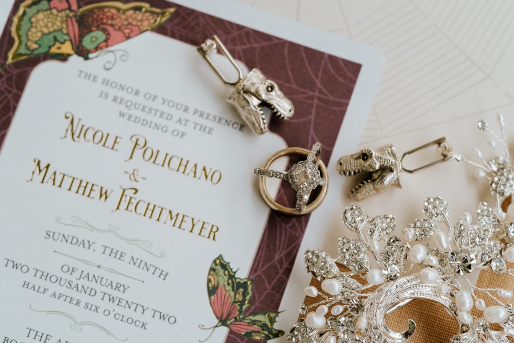 Macro detail of wedding rings and t-rex dinosaur cufflinks on top of wedding invitation.