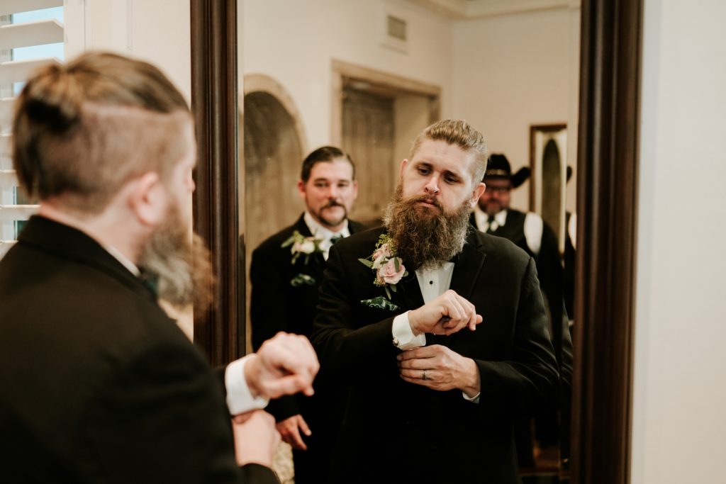 Reflection of groom adjusting cufflinks in mirror with groomsmen